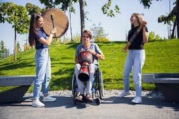 Foto grátis feliz homem deficiente em uma cadeira de rodas, passando um tempo com amigos tocando música instrumental ao vivo ao ar livre.