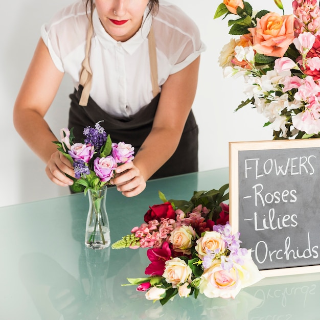 Foto grátis florista feminina organizando flores em um vaso na mesa de vidro