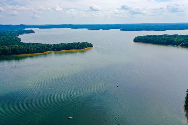 Foto aérea de barcos viajando pelo lago com árvores e céu nublado