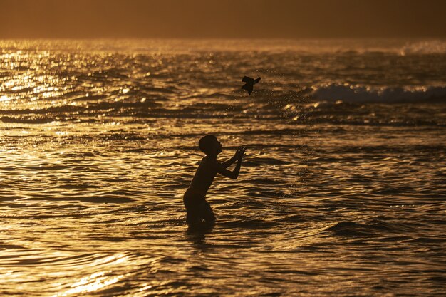 Foto da silhueta de um menino brincando na praia