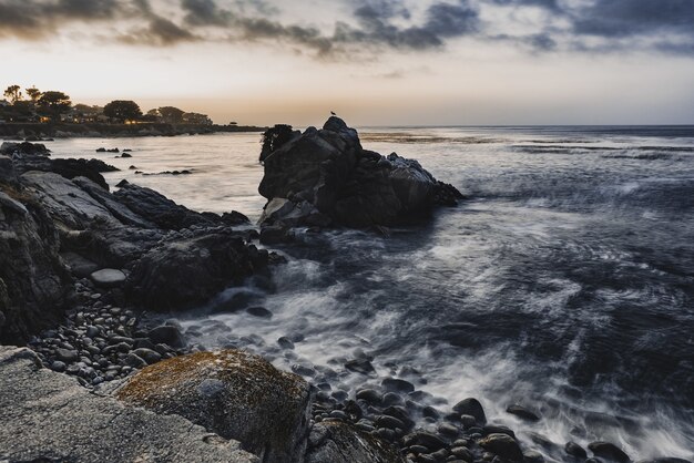 Foto de ângulo alto de pequenas pedras na costa do mar sob o céu nublado da noite