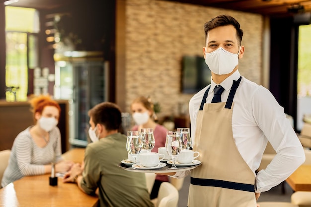 Foto grátis garçom feliz servindo café para seus clientes enquanto usava máscara facial protetora em um café