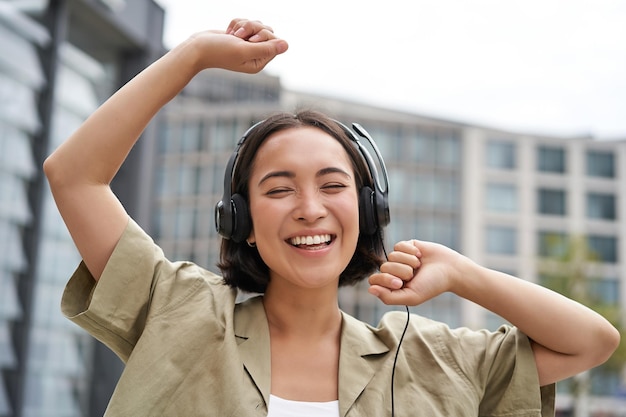 Garota dança na rua com fones de ouvido ouve música e se sente feliz andando na cidade