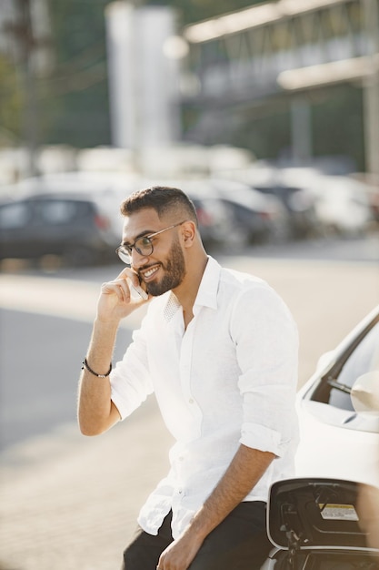 Homem com conversa móvel enquanto espera o carro elétrico. Estação de recarga, carros ecológicos.