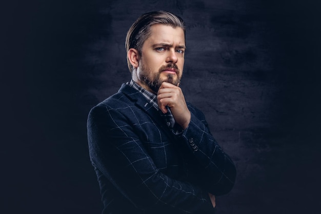 Foto grátis homem de meia idade pensativo com barba e penteado vestido com um elegante terno azul em um fundo escuro texturizado no estúdio.