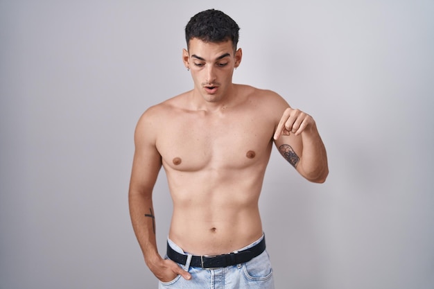 Foto grátis homem hispânico bonito de pé sem camisa apontando para baixo com os dedos mostrando publicidade rosto surpreso e boca aberta