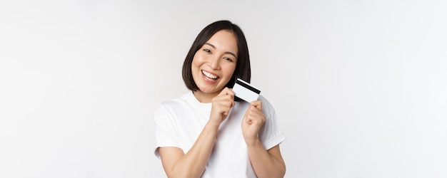 Foto grátis imagem de mulher asiática sorridente abraçando cartão de crédito comprando sem contato em camiseta branca sobre fundo branco