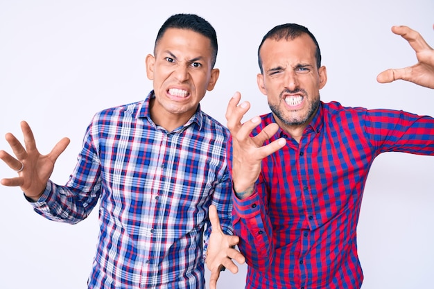 Foto grátis jovem casal gay de dois homens vestindo roupas casuais gritando frustrados de raiva, mãos tentando estrangular, gritando loucos