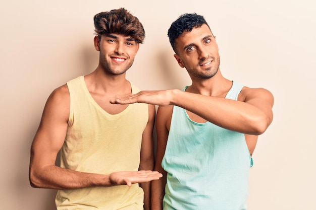 Foto grátis jovem casal gay vestindo roupas casuais, gesticulando com as mãos mostrando símbolo de medida de sinal de tamanho grande e grande sorrindo olhando para o conceito de medição da câmera