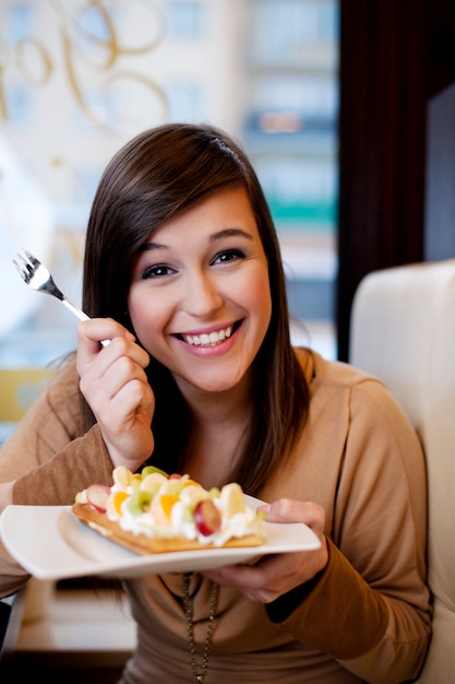 Jovem comendo waffles com chantilly e frutas