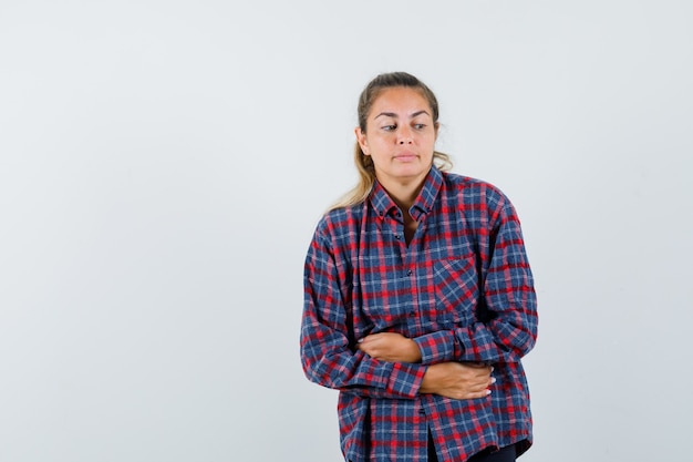 Jovem de camisa xadrez com dor de barriga e parecendo cansada