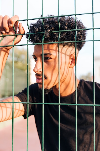 Foto grátis jovem étnico pensativo por trás da cerca