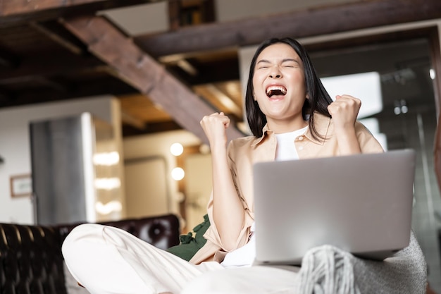 Foto grátis jovem garota asiática triunfante vencendo reagindo feliz com laptop notificação de boas notícias gritando sim