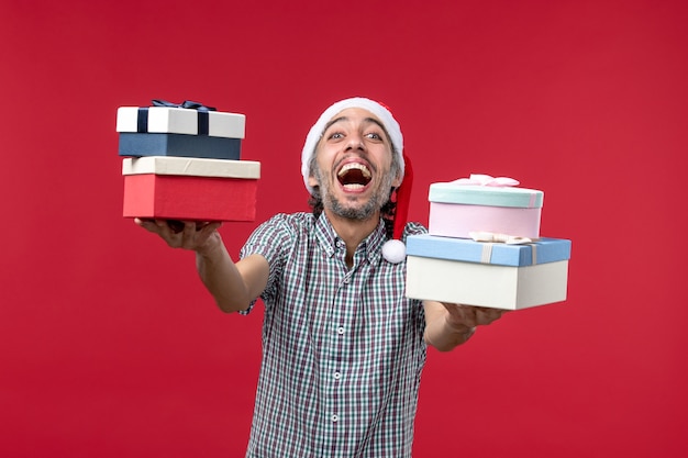 Foto grátis jovem homem de frente feliz segurando presentes em fundo vermelho