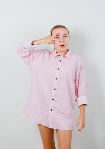 Foto grátis jovem mostrando o sinal v no olho com uma camisa rosa e bonita