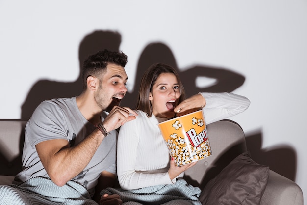 Foto grátis jovem mulher assistindo tv e comendo pipoca perto de homem no sofá