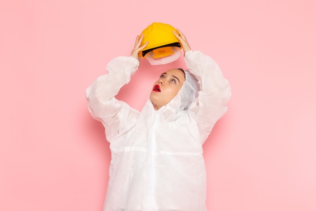 Foto grátis jovem mulher bonita em um terno branco especial e tirando o capacete amarelo na rosa