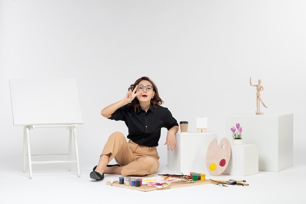 Foto grátis jovem mulher sentada de frente na sala com tintas borla e cavalete em fundo branco