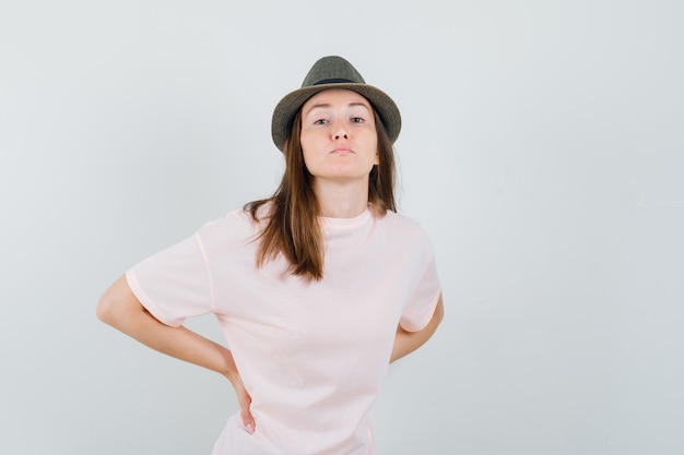 Foto grátis jovem mulher tendo dor nas costas em t-shirt rosa, chapéu e parecendo exausta, vista frontal.