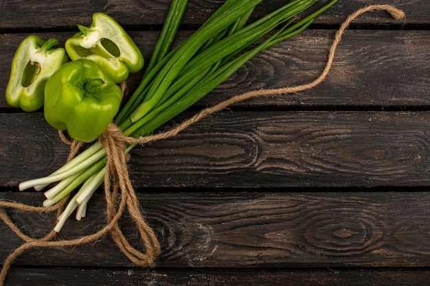 Foto grátis legumes cortados pimentões verdes, juntamente com ervas verdes amarradas em uma mesa de madeira rústica marrom