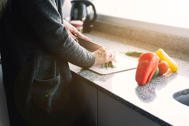 Legumes de corte de mão de mulher no balcão da cozinha