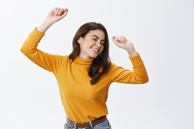 Foto grátis linda mulher dançando e se divertindo com os olhos fechados e sorriso despreocupado curtindo festa e música em pé feliz contra fundo branco