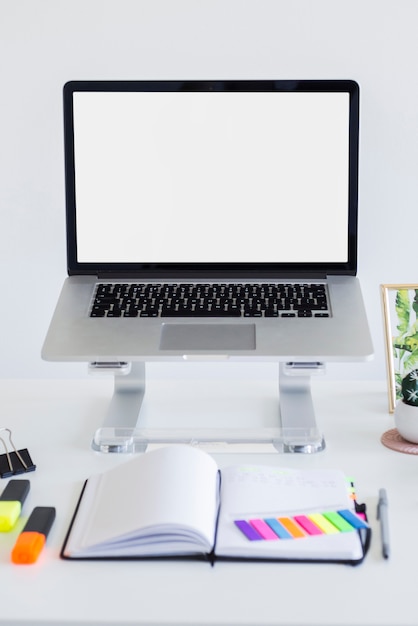 Local de trabalho com o laptop no carrinho perto de notebook, marcadores e adesivos