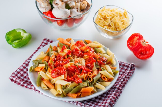 Macarrão penne com cogumelos, tomate, molho, pimenta, macarrão cru em um prato