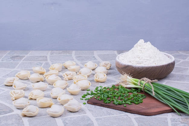 Foto grátis massas khinkali cruas na farinha com um ramo de cebola verde.