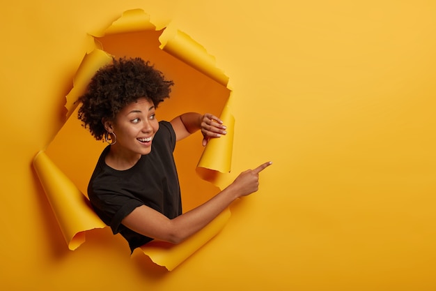 Menina alegre e sorridente, de aparência amigável, aponta para o lado com expressão feliz, sorriso dentuço, satisfeita em mostrar propaganda incrível