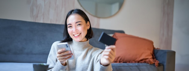 Foto grátis menina asiática sorridente com smartphone e cartão de crédito faz compras on-line e usa telefone celular para