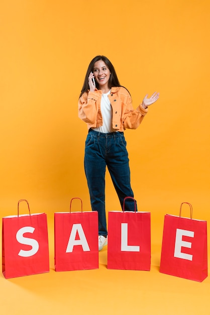 Foto grátis mulher animada falando ao telefone atrás de sacolas de compras em promoção