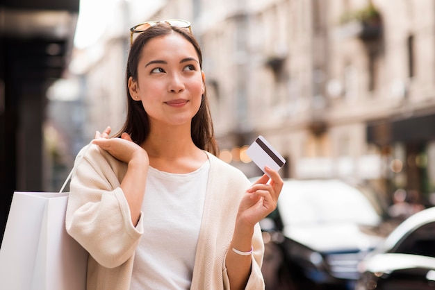 Mulher ao ar livre segurando um cartão de crédito e uma sacola de compras