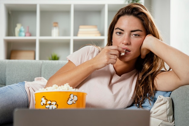 Foto grátis mulher comendo pipoca enquanto olha para o laptop