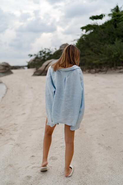 Mulher elegante com roupa casual azul posando na praia solitária em nublado xAweather Vista de trás