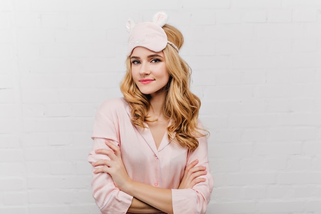 Foto grátis mulher elegante de olhos azuis e pijama de seda, posando com os braços cruzados. fascinante garota encaracolada em máscara de dormir em pé em pose confiante.