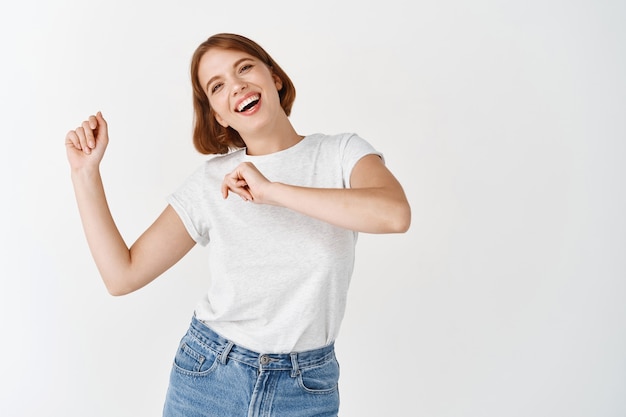 Foto grátis mulher feliz dançando e se divertindo, rindo de alegria, encostada na parede branca