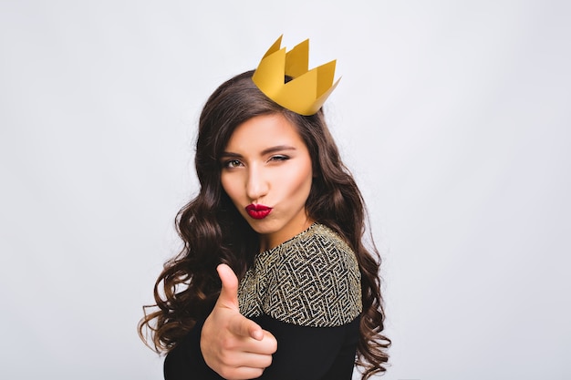 Foto grátis mulher lúdica do retrato na coroa amarela se divertindo. mulher incrível jovem animada, vestido preto de luxo, cabelo castanho encaracolado longo, emoções sérias. festa de ano novo, aniversário, brincar.