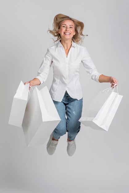 Mulher sorridente pulando e posando enquanto segura várias sacolas de compras