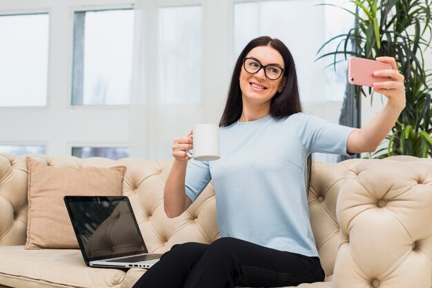 Mulher tomando selfie com café no sofá