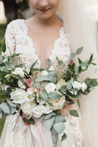 Noiva do lindo vestido detém um buquê de noiva com eucalipto e rosas brancas