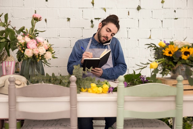 Foto grátis ocupado florista masculina tendo ordem no telefone móvel e escrevê-lo no notebook