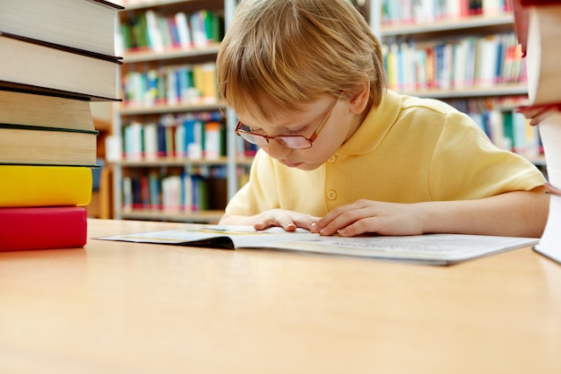 Foto grátis rapaz pequeno com óculos de leitura na biblioteca