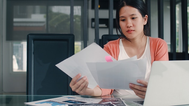 Foto grátis registros asiáticos novos da mulher gravida das receitas e despesas em casa. menina mãe feliz usando orçamento de registro de laptop, impostos, documento financeiro, comércio eletrônico, trabalhando na sala de estar em casa.