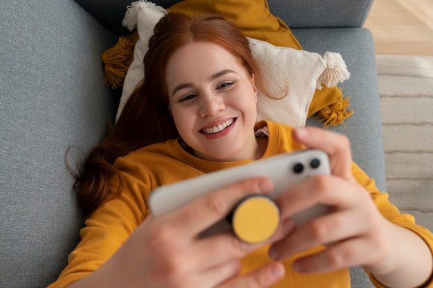 Foto grátis retrato de mulher usando seu smartphone em casa no sofá, segurando na tomada pop