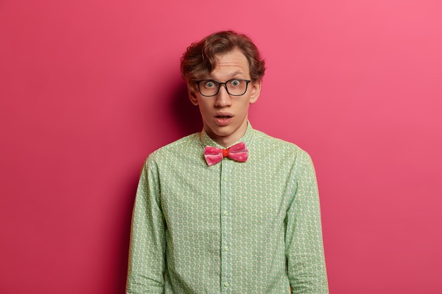 Foto grátis retrato de um jovem professor estupefato e chocado olhando através de óculos transparentes, vestido formalmente, envergonhado por receber uma tarefa inesperada para o projeto, expressa surpresa e descrença, posa em ambientes internos