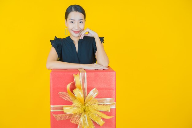 Retrato de uma bela jovem asiática sorrindo com caixa de presente vermelha em amarelo