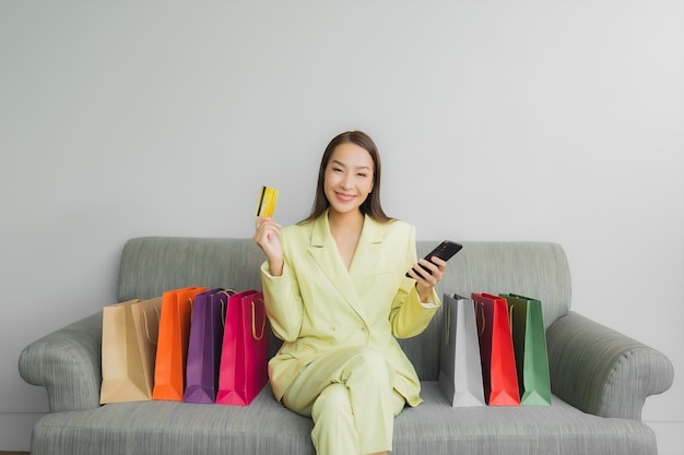 Foto grátis retrato de uma bela jovem asiática usando computador portátil com cartão de crédito para compras online no sofá no interior da sala de estar