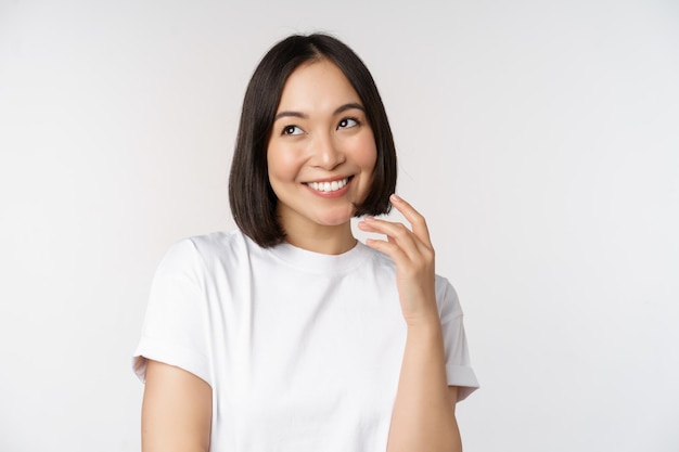 Foto grátis retrato de uma linda mulher coquete rindo e sorrindo olhando de lado pensando pensativo ou imaginando algo em camiseta branca sobre fundo de estúdio