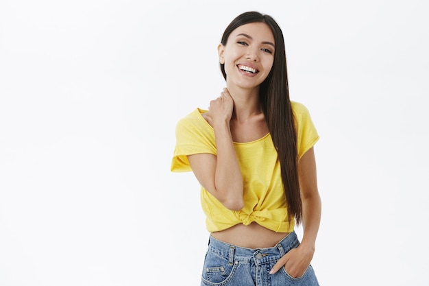 Foto grátis retrato de uma mulher alegre e amigável e extrovertida, com cabelo escuro, em uma elegante camiseta amarela segurando a mão no bolso